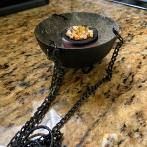 A picture of lit charcoal with resin on top in a mini cauldron.